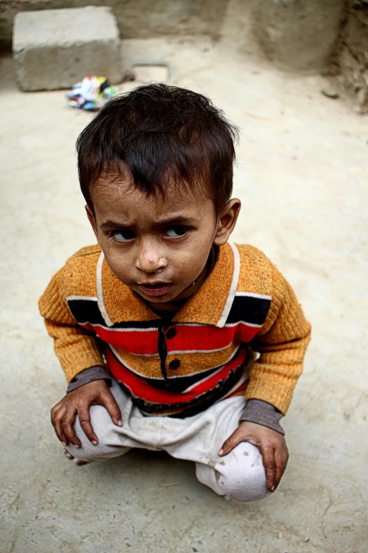 a small child sitting on the ground looking at the camera, by Riza Abbasi, slide show, worn, sickly, full frame image