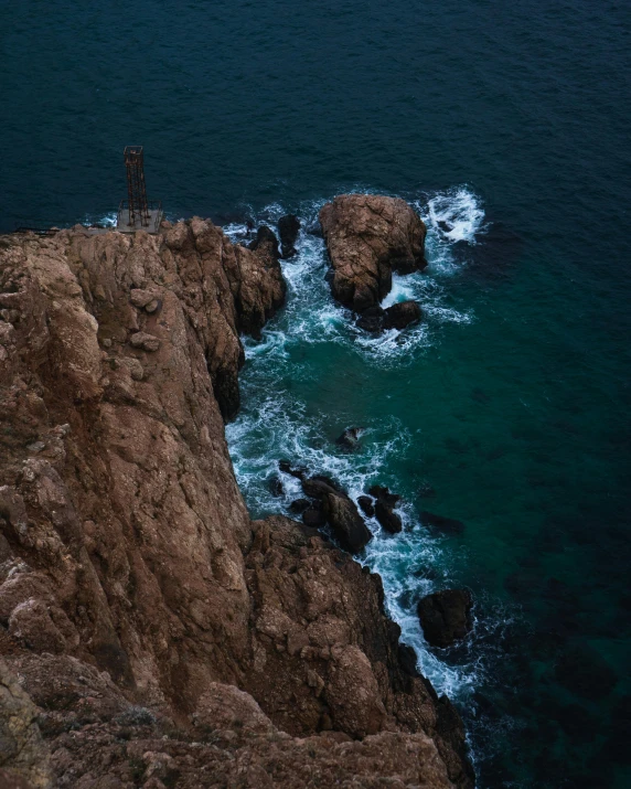 a man standing on top of a cliff next to the ocean, by Elsa Bleda, pexels contest winner, australian tonalism, brown and cyan color scheme, multiple stories, high view, granite