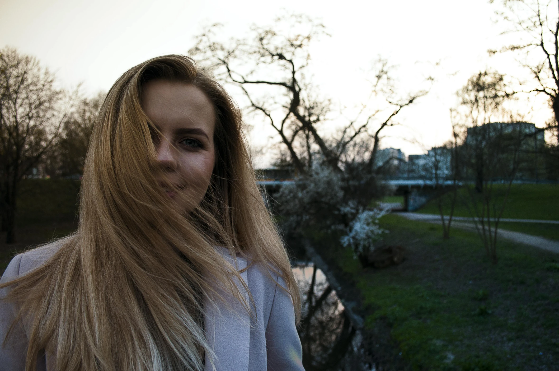 a woman standing next to a body of water, a picture, by Niko Henrichon, pexels contest winner, brown-blond-hair pretty face, spring evening, in a city park, low quality footage