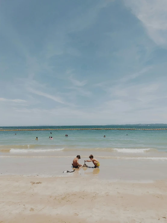 a couple of people sitting on top of a sandy beach, by Arabella Rankin, unsplash contest winner, minimalism, manly, shallow waters, kids playing, 🌸 🌼 💮