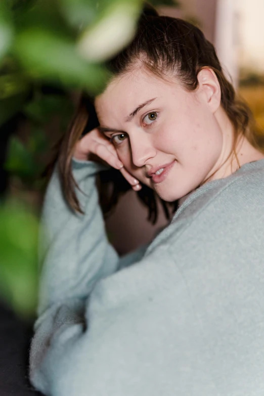 a woman sitting on top of a couch next to a plant, by Sven Erixson, unsplash, wearing sweatshirt, alluring plus sized model, headshot profile picture, 19-year-old girl