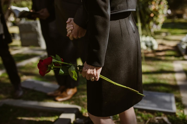 a woman in a black dress holding a red rose, by Carey Morris, pexels, symbolism, graveside, a man wearing a black jacket, woman holding another woman, head down