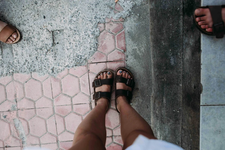 a couple of people standing next to each other on a sidewalk, by Niko Henrichon, unsplash, birkenstock sandals, background image, wide high angle view, wearing a brown