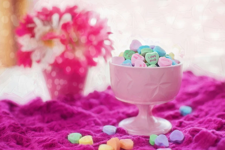 a pink bowl filled with conversation hearts next to a vase of flowers, a pastel, pixabay contest winner, 🎀 🗡 🍓 🧚, a table full of candy, blurred, purple