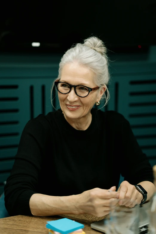 a woman sitting at a table in front of a laptop computer, photorealism, straight grey hair, award-winning style, dark. no text, annie lebowitz