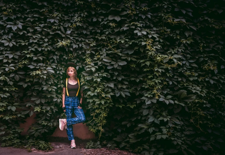 a woman standing in front of a wall of leaves, an album cover, inspired by Elsa Bleda, pexels contest winner, wearing overalls, green legs, better known as amouranth, trending on 500px