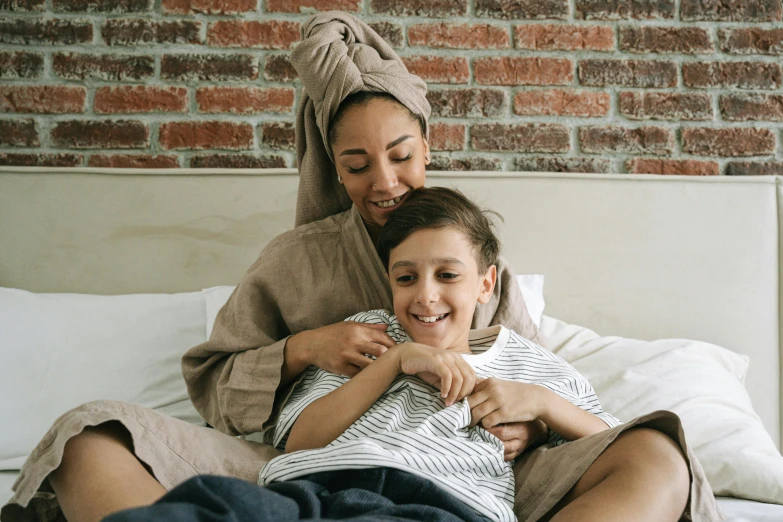 a woman sitting on top of a bed next to a child, pexels contest winner, happening, wearing a towel, cuddling, brown robes, bedhead