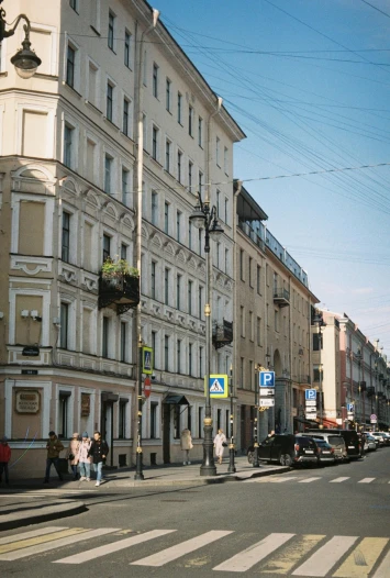 a group of people walking down a street next to tall buildings, a photo, inspired by Illarion Pryanishnikov, house's and shops and buildings, neoclassical, seen from the side, street elevation