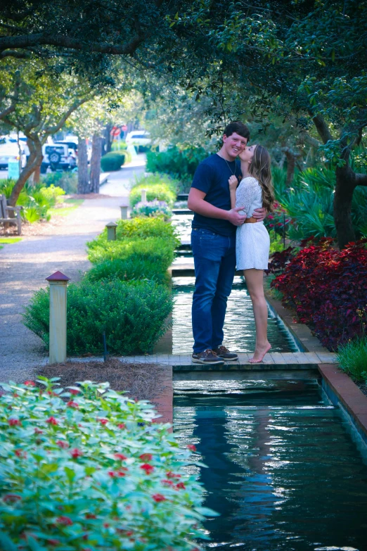 a man and a woman standing next to a pond, lush garden surroundings, in savannah, street pic, kissing