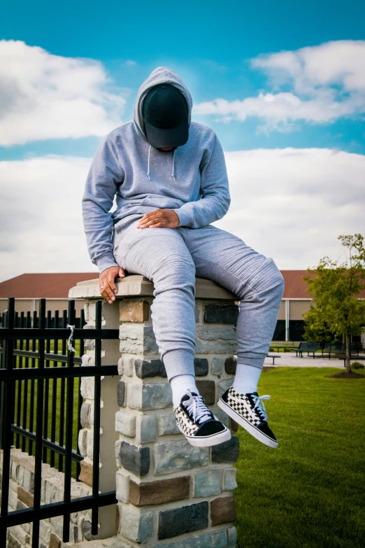 a man sitting on top of a brick wall, an album cover, inspired by Jordan Grimmer, trending on pexels, grey hoodie, 15081959 21121991 01012000 4k, leg shot, at a park