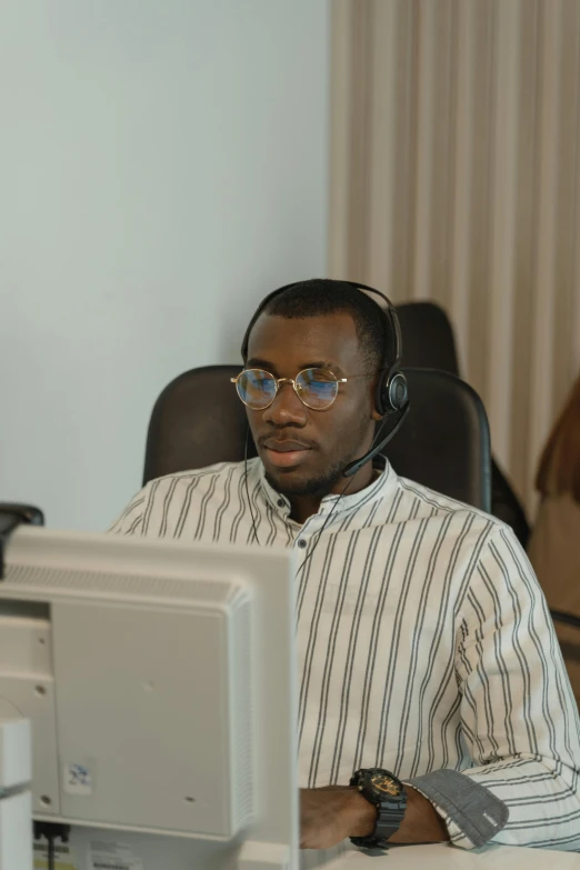 a man sitting at a desk in front of a computer, working in a call center, emmanuel shiru, colour corrected, looking content