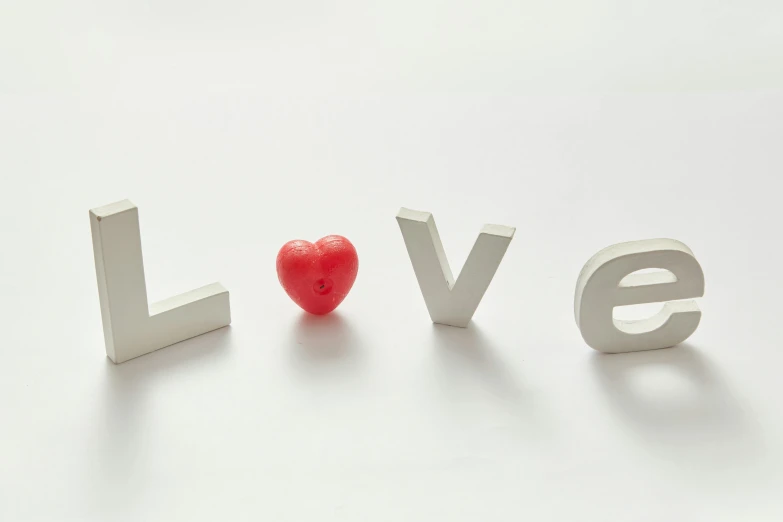 a red heart sitting next to the word love, letterism, soft white rubber, colour photograph, silver，ivory, white