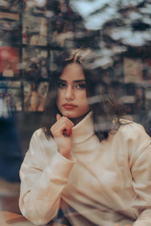 a woman sitting at a table in front of a window, a picture, inspired by Elsa Bleda, trending on pexels, square face, young middle eastern woman, girl in a record store, low quality photo