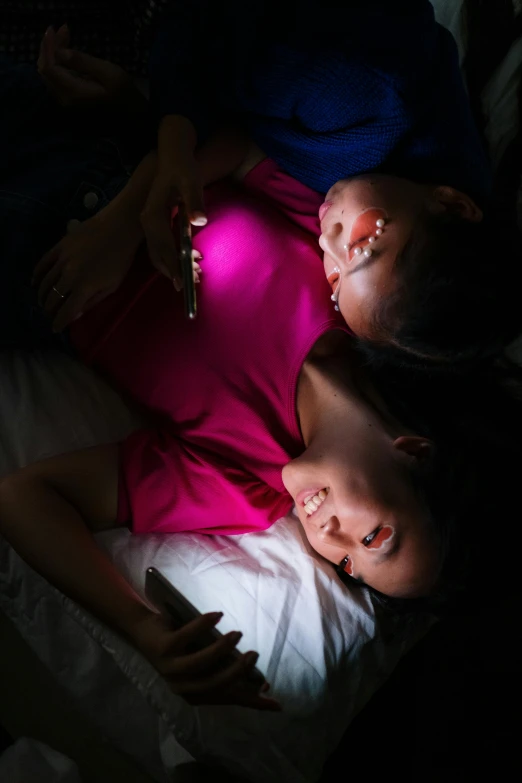 a couple of kids laying on top of a bed, a portrait, trending on pexels, flashlight on, asian women, glowing screens, lesbian embrace