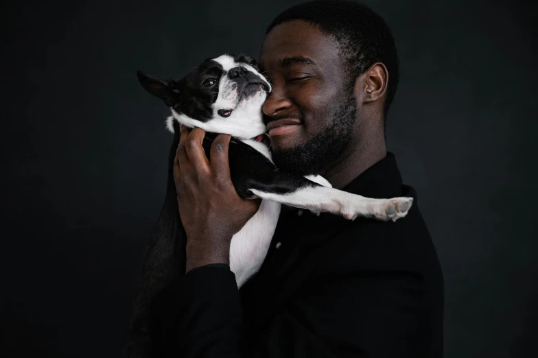 a man holding a small black and white dog, by Winona Nelson, pexels contest winner, renaissance, ( ( dark skin ) ), plain background, bowater charlie and brom gerald, jaylen brown