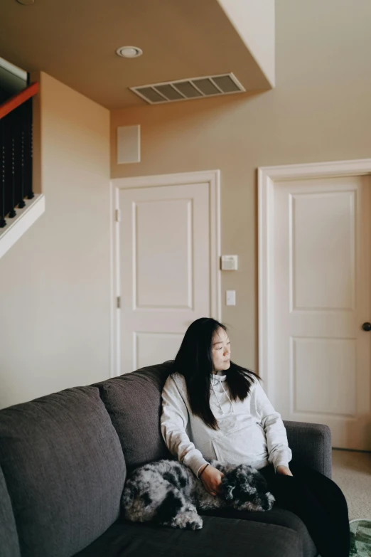 a woman sitting on a couch in a living room, by helen huang, unsplash, slanted ceiling, low quality photo, about to enter doorframe, asian descent