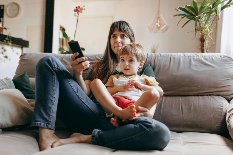 a woman sitting on a couch holding a child, a cartoon, pexels, phone photo, television still, avatar image, maintenance