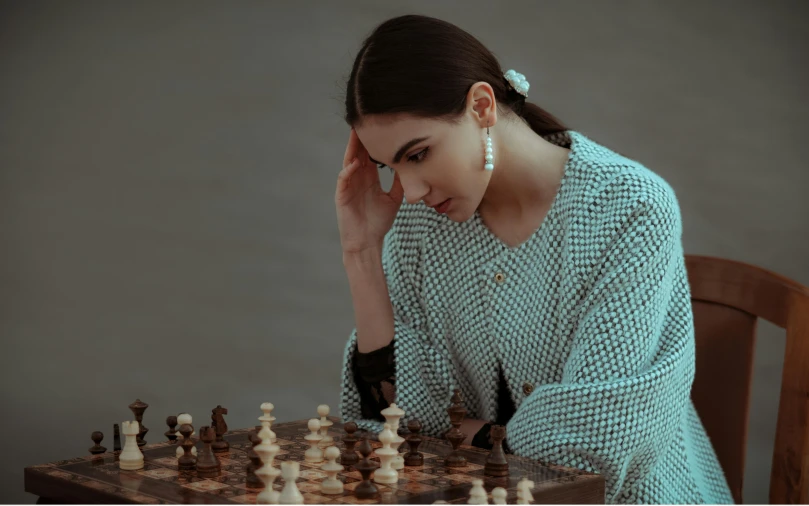 a woman sitting at a table playing a game of chess, a colorized photo, by Emma Andijewska, pexels contest winner, classical realism, wearing a track suit, wearing silver silk robe, thoughtful ), sophisticated young woman
