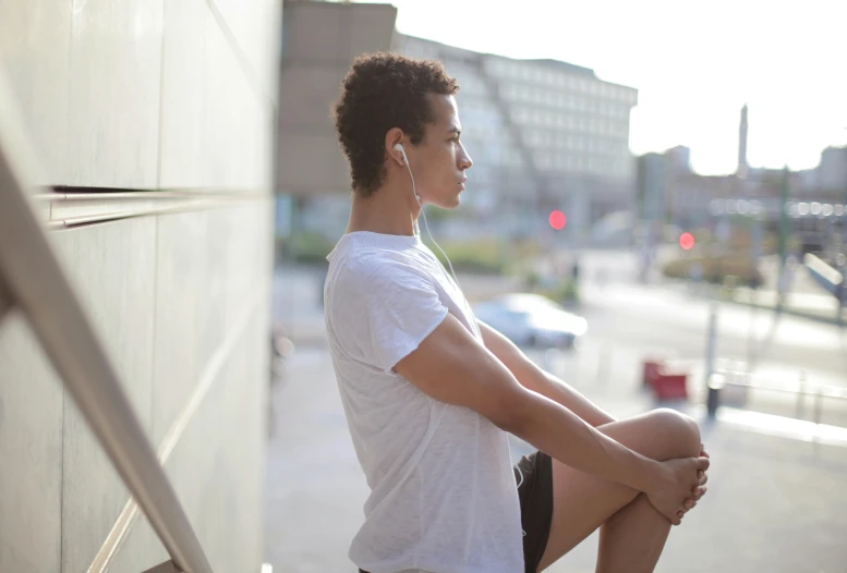 a woman sitting on a ledge with headphones on, happening, man in white t - shirt, profile pose, wearing fitness gear, curly haired