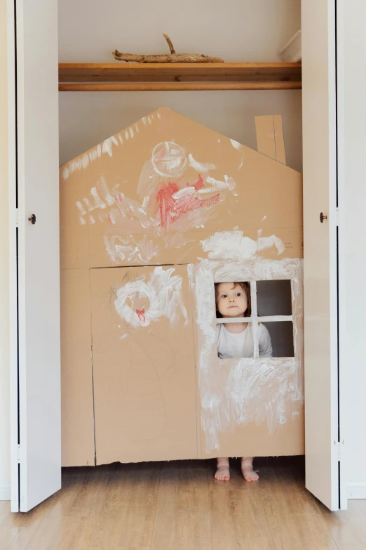 a child standing in front of a cardboard house, inspired by Rachel Whiteread, unsplash, conceptual art, exiting from a wardrobe, full view of face and body, paint, indoor scene