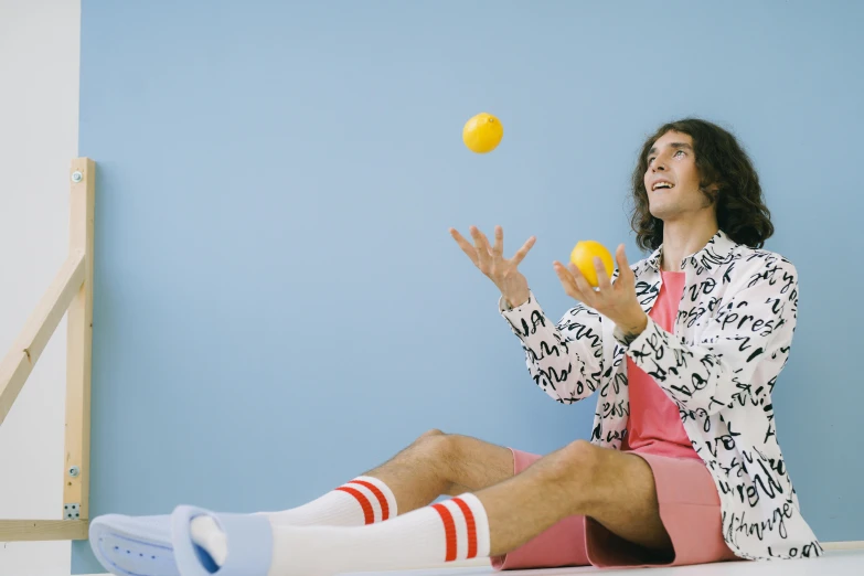 a man sitting on the floor playing with a ball, by Julia Pishtar, wearing a lemon, performing a music video, paddle and ball, avatar image