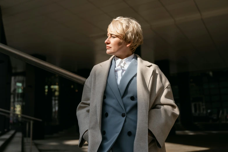 a man in a suit and tie standing in front of a building, inspired by Alexander Roslin, trending on pexels, short platinum hair tomboy, woman is in a trenchcoat, female lawyer, thumbnail