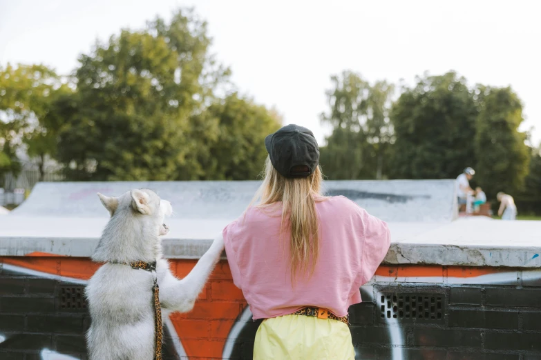 a woman standing next to a dog on a skateboard ramp, trending on unsplash, graffiti, view from back, wes anderson style, best friends, wearing hi vis clothing