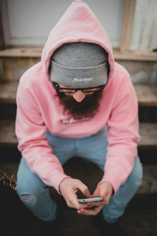 a man in a pink hoodie looking at his cell phone, by Pamela Drew, trending on pexels, wearing a light grey crown, denim, archwizzard in a hat, head straight down