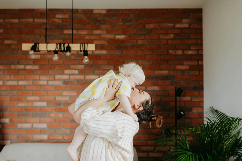 a woman holding a baby in her arms, pexels contest winner, high ceilings, brick, avatar image, cottagecore hippie