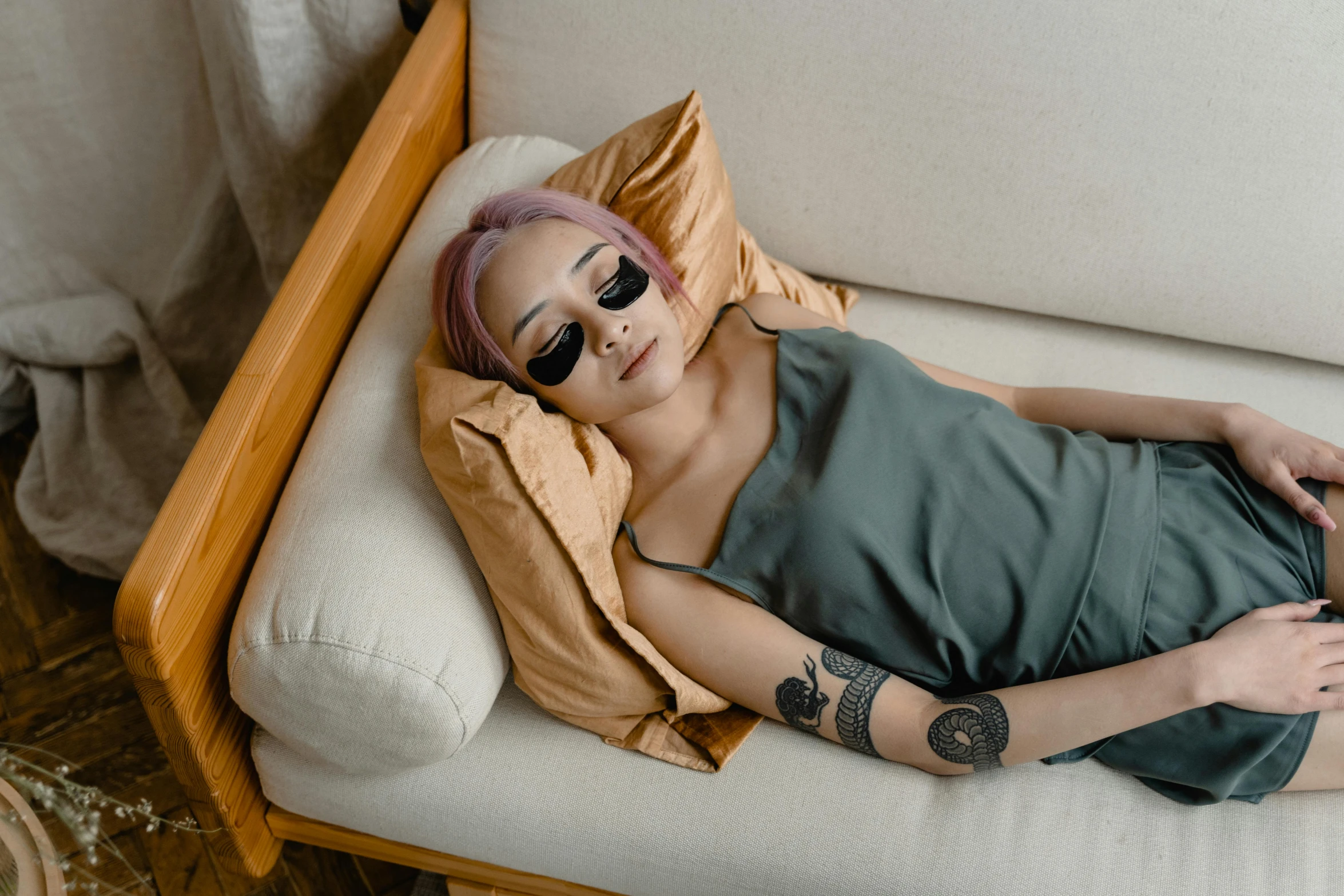 a woman with pink hair laying on a couch, a tattoo, inspired by Elsa Bleda, trending on pexels, visual art, with sunglass, asian women, small bed not made, with grey skin