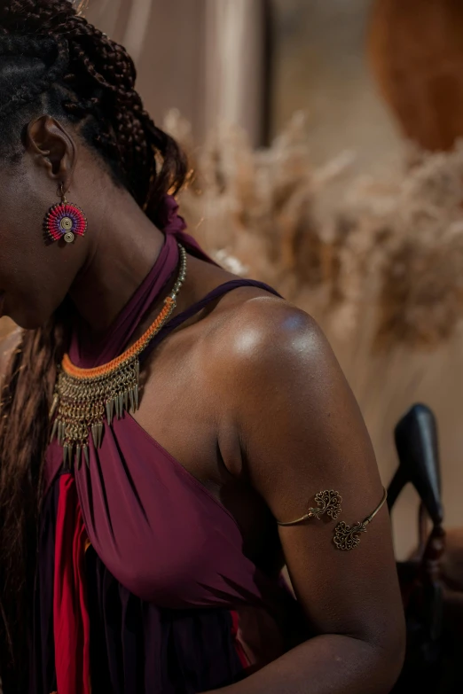 a woman in a purple dress holding a cell phone, inspired by Ras Akyem, trending on pexels, afrofuturism, red and golden color details, himba hairstyle, showing her shoulder from back, bracelets and necklaces