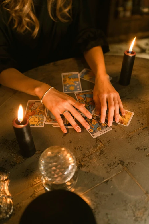 a woman sitting at a table with candles and playing cards, trending on pexels, renaissance, a sorcerer casting a fireball, a seance, instagram post, hands on counter