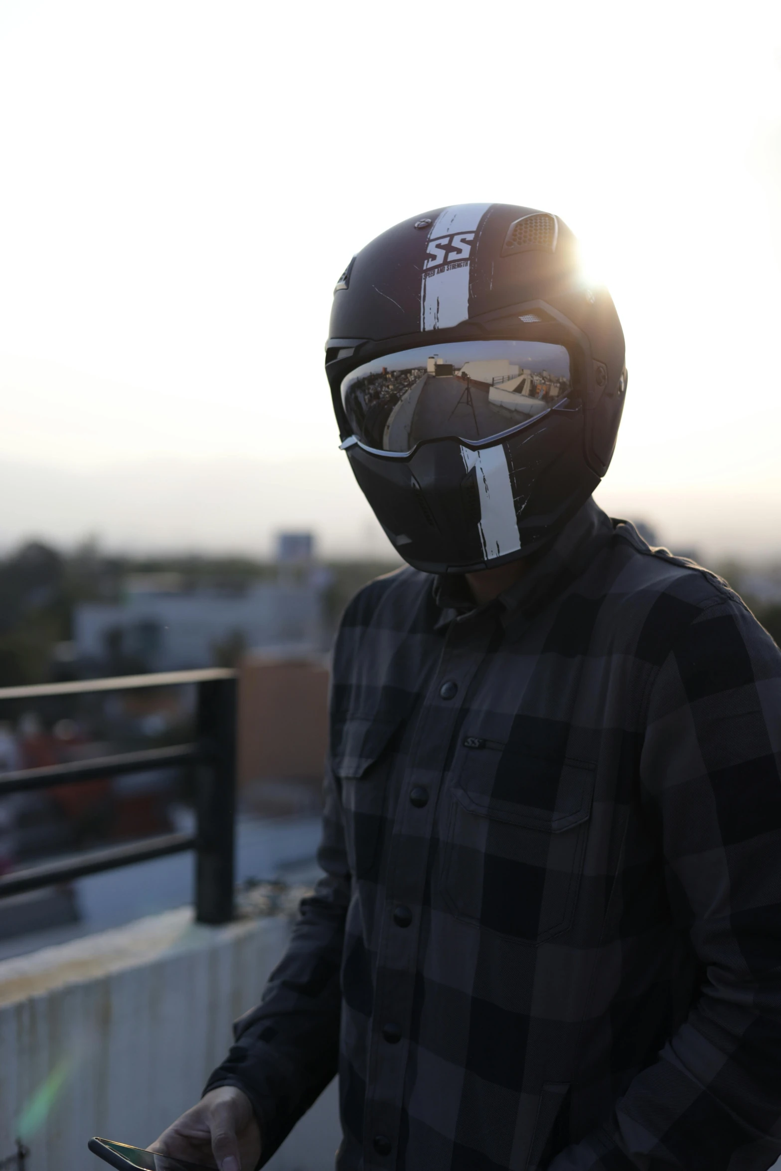 a man standing on top of a roof holding a cell phone, inspired by Alonso Vázquez, featured on reddit, motorcycle helmet, wearing facemask and sunglasses, **cinematic, sk