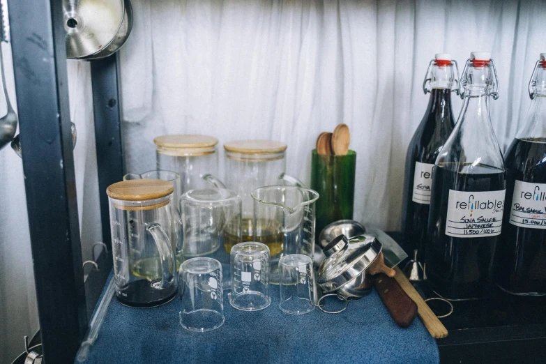 a shelf filled with bottles and glasses on top of a blue table, inspired by Ceferí Olivé, unsplash, inside a glass jar, product view, disassembled, highly detailded