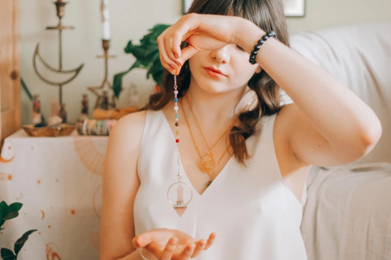 a woman in a white top sitting on a couch, a photo, by Julia Pishtar, trending on pexels, occult jewelry, wind chimes, gemstone forehead, holding an epée