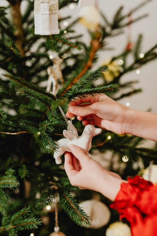 a woman decorating a christmas tree with ornaments, by Julia Pishtar, pexels, folk art, holding origami qilin, detail shot, natural soft light, ceramic