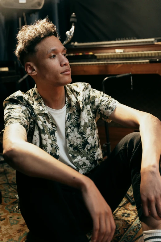 a man sitting on the floor in front of a piano, wearing a shirt, wlop and ross tran, looking to the side off camera, patterned clothing