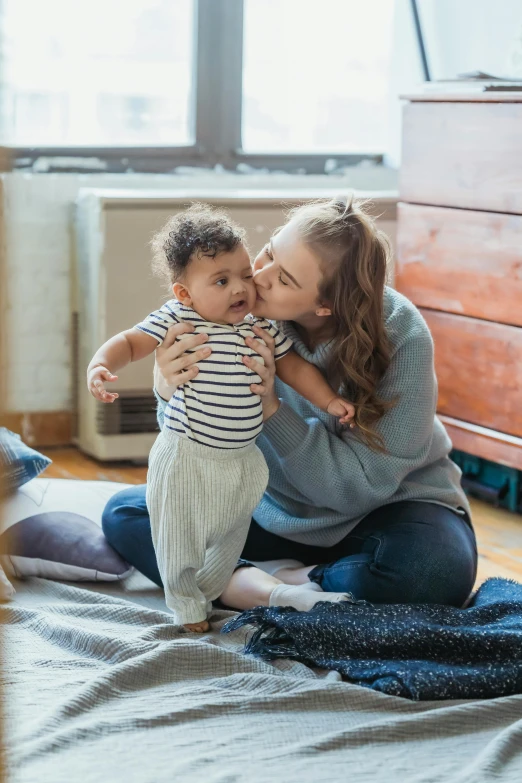 a woman sitting on top of a bed holding a baby, pexels contest winner, renaissance, kissing each other, in a living room, varying ethnicities, cute boy