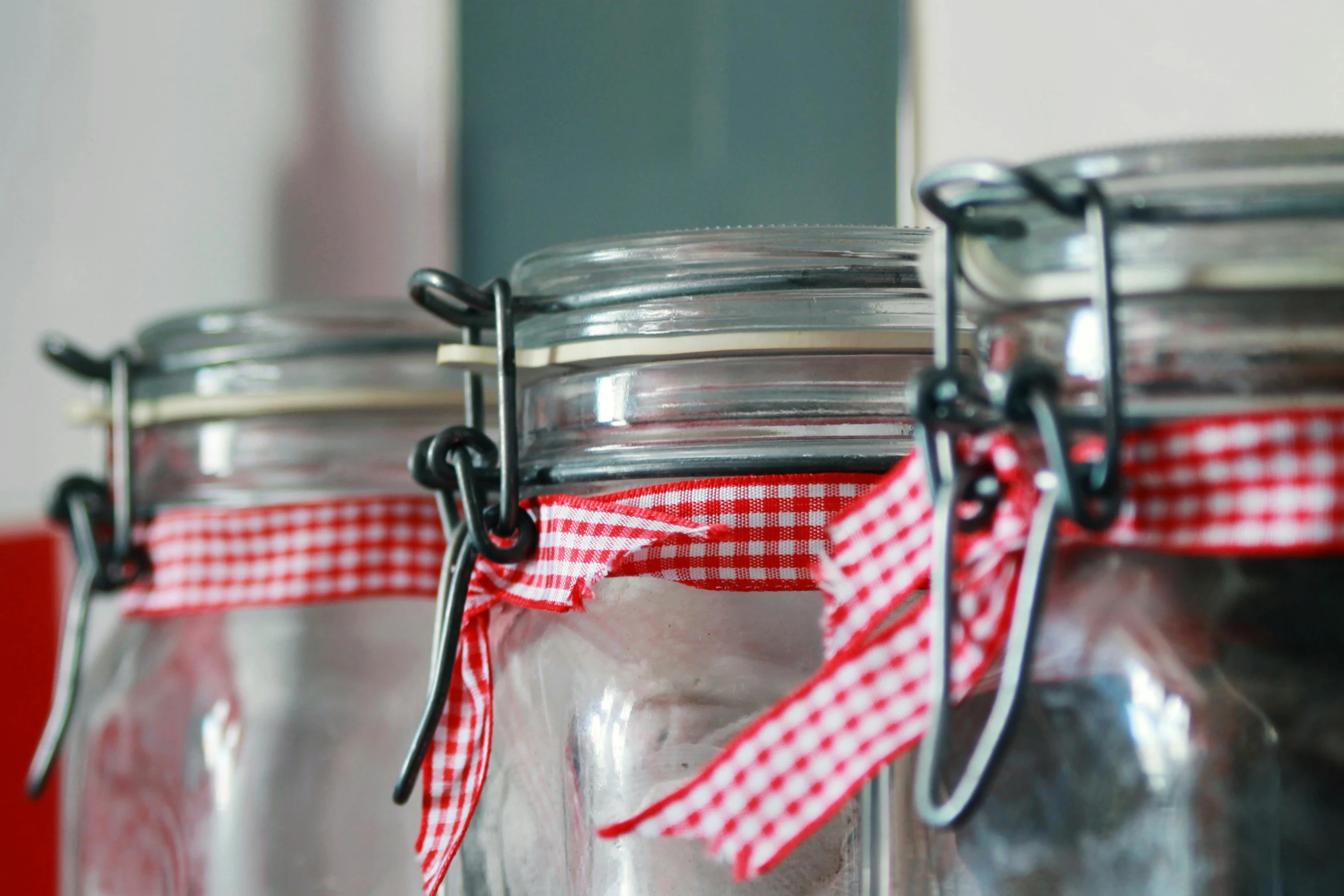 a couple of glass jars sitting on top of a table, a picture, red ribbon, cupboards, up close, maintenance