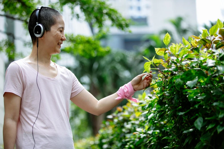 a woman standing next to a bush with headphones on, inspired by Wen Zhenheng, happening, biodiversity all round, gardening, headset, schools