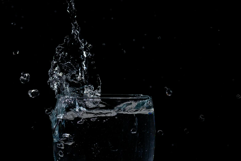 a glass filled with water sitting on top of a table, by Jan Rustem, pexels, photorealism, water splashing cascading, with a black background, splash image, bottom shot