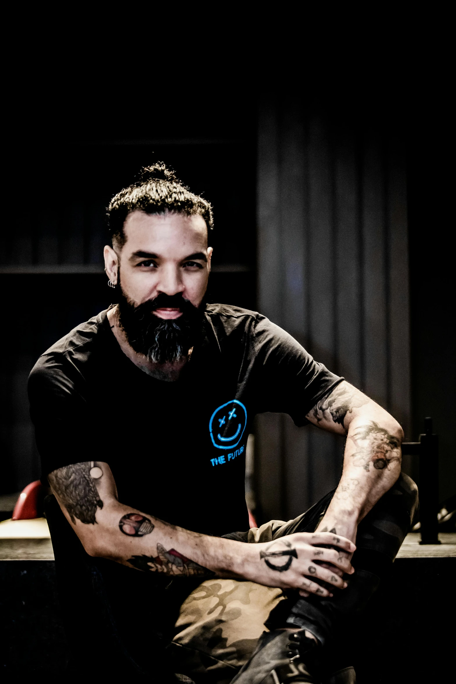 a man with a beard sitting on a counter, a tattoo, with a beard and a black shirt, joel torres, headshot, avatar image