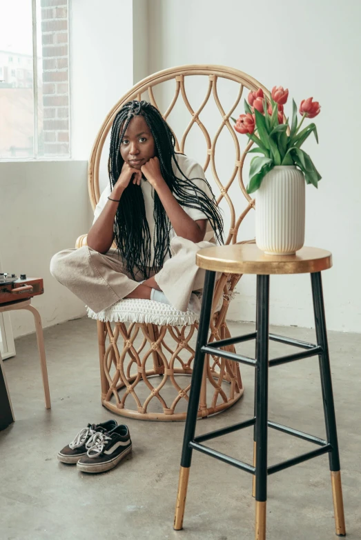 a woman sitting in a chair next to a vase of flowers, pexels contest winner, black arts movement, box braids, wearing white sneakers, official store photo, long flowing braided hair