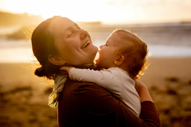 a woman holding a baby on top of a beach, pexels contest winner, smiling laughing, golden hour scene, profile image, decorative