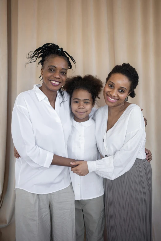 a family posing for a picture in front of a curtain, by Lily Delissa Joseph, pexels, renaissance, light skinned african young girl, wearing a white shirt, lesbian, in front of white back drop