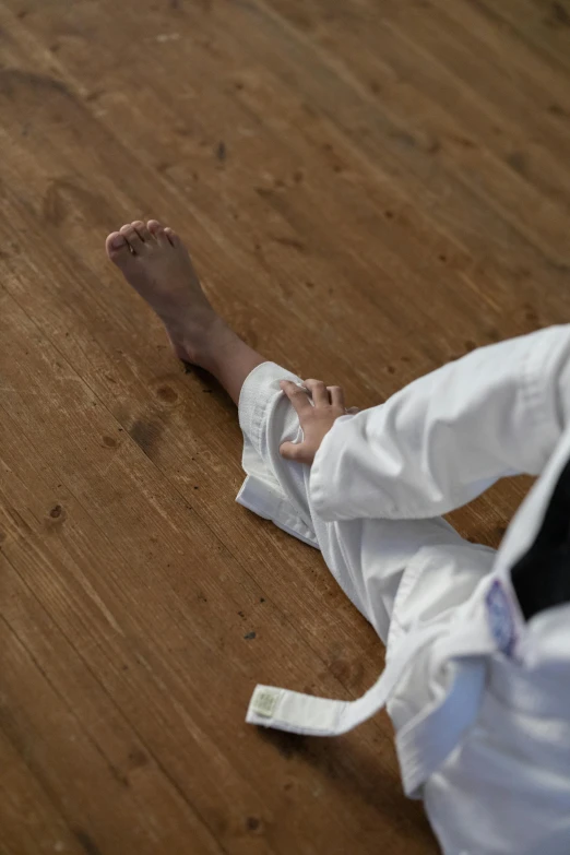 a close up of a person on a wooden floor, inspired by Kanō Shōsenin, white, karate, recovering from pain, high-angle