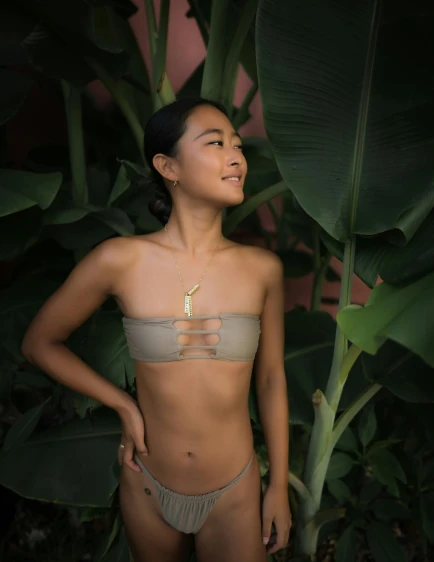 a woman in a bikini standing in front of a banana tree, inspired by Ruth Jên, unsplash, sumatraism, low quality photo, bone jewelry, posing together in bra, soft lighting from above