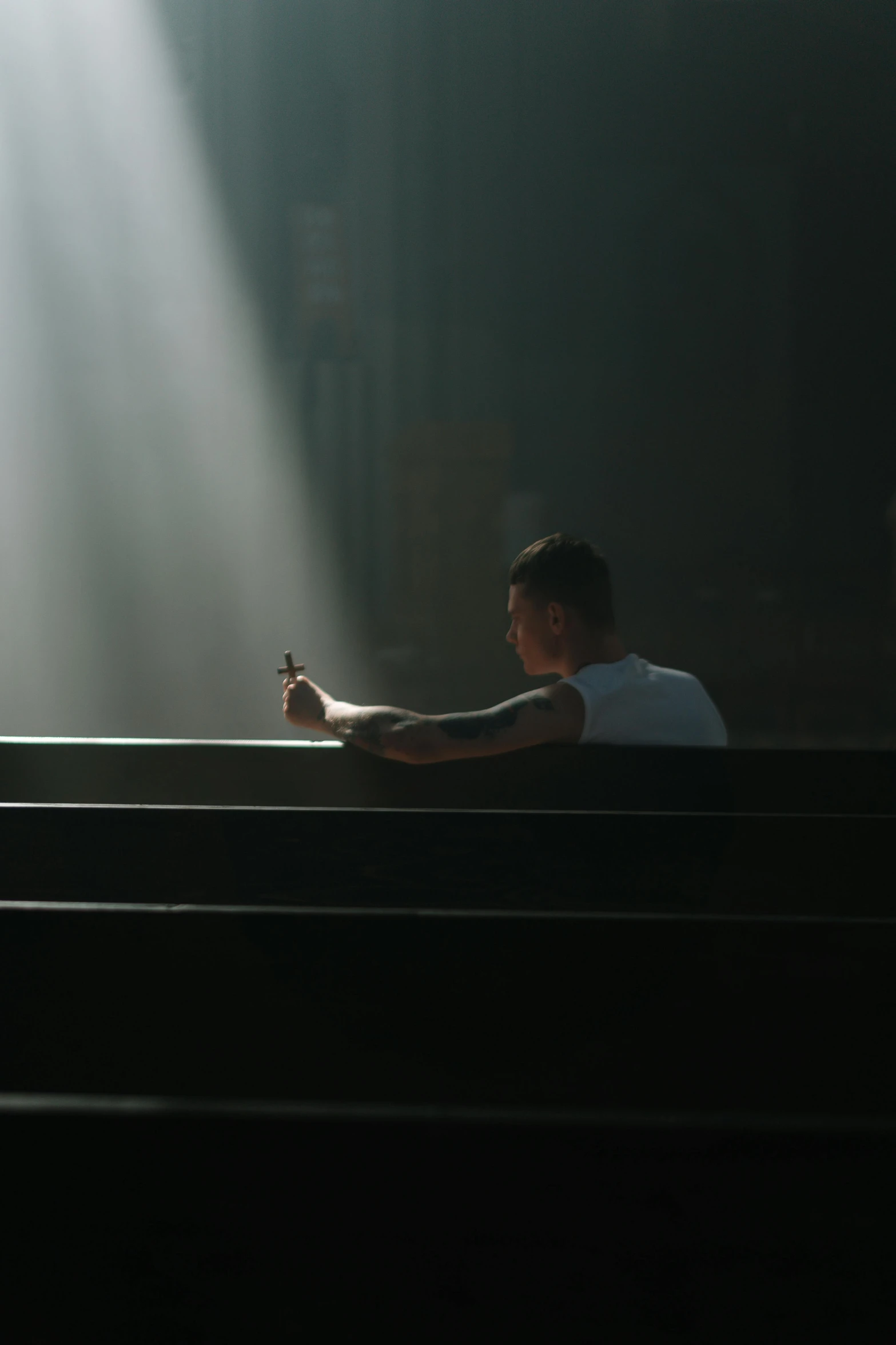 a man sitting on a bench in a dark room, bursting with holy light, looking at his phone, sacrament, trending photo