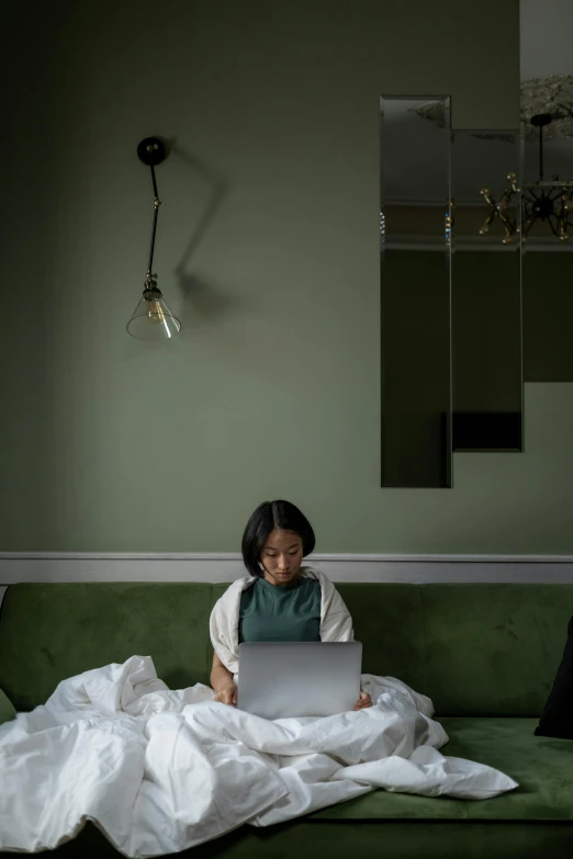 a woman sitting on a couch using a laptop, a portrait, inspired by Elsa Bleda, pexels contest winner, renaissance, green robe, sitting on the edge of a bed, asian descent, slightly minimal