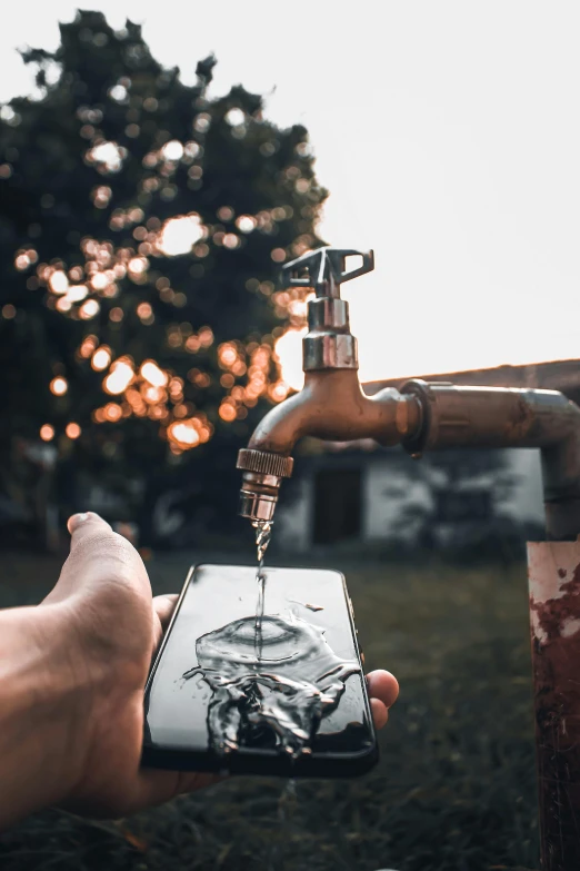 a person holding a cell phone next to a faucet, a picture, pexels contest winner, al fresco, made of water, brown, magic hour